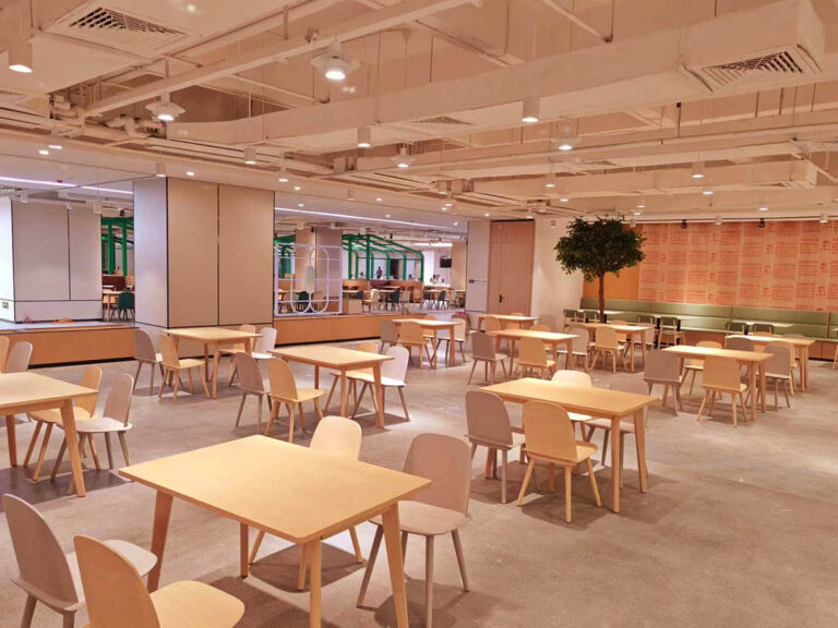 Open canteen dining area with light wood tables and wall bench seating by Dejell