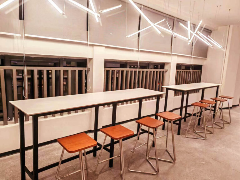 Wall-mounted bar tables with wood-top stools in company canteen by Dejell